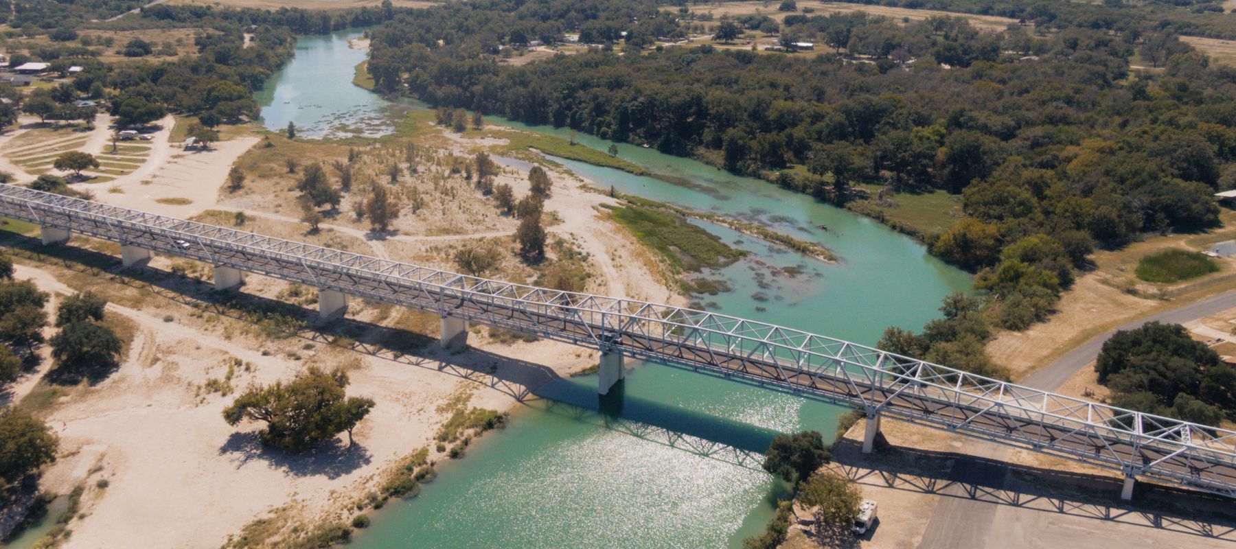 Aerial view of a steel bridge crossing over the green waters of the Llano River in Junction, Texas
