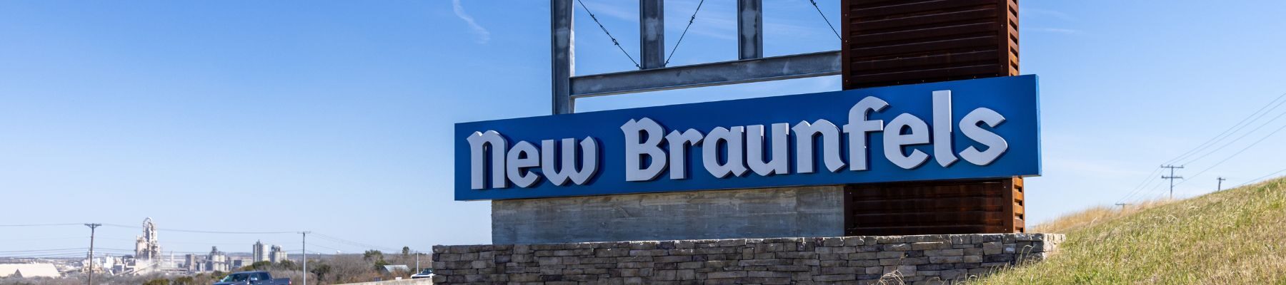 A large roadside sign welcoming visitors to New Braunfels, Texas, under a clear blue sky
