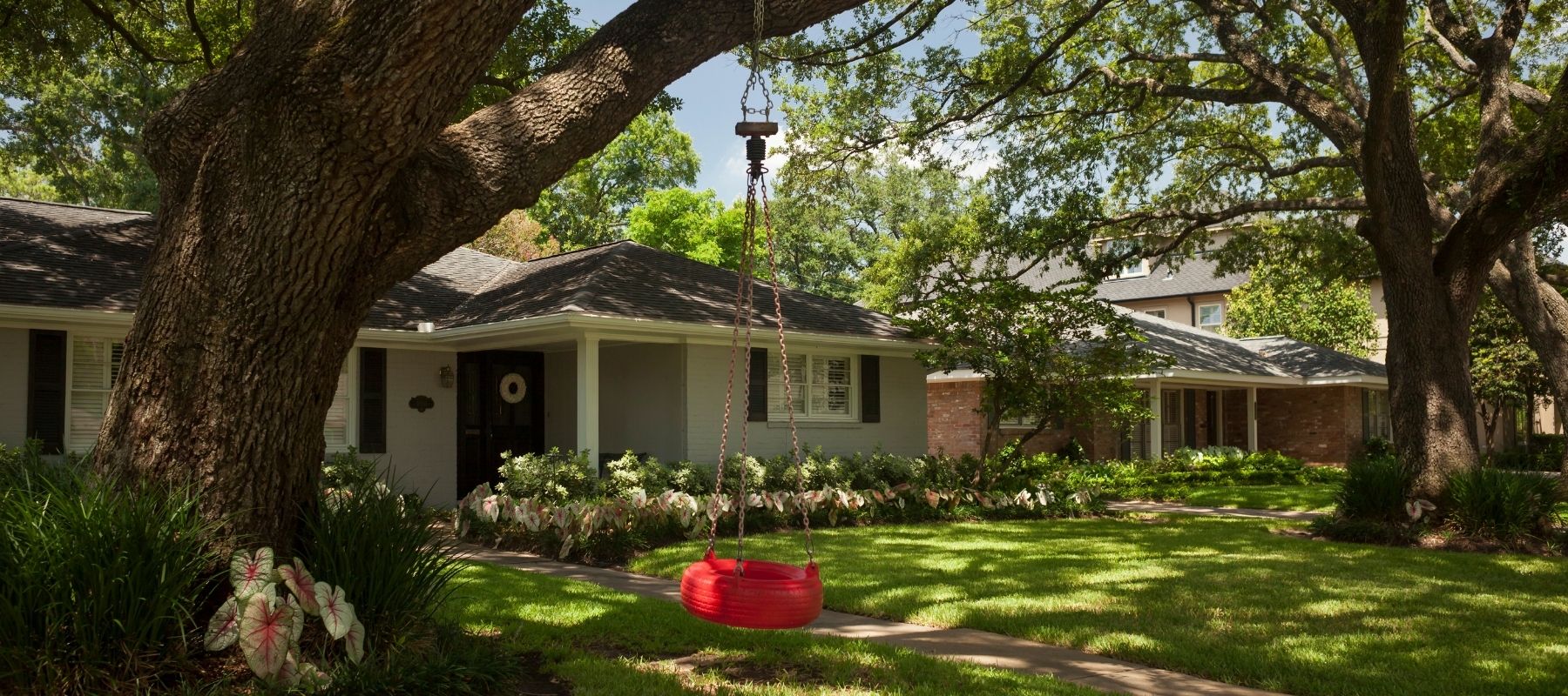Single-story suburban home with large oak trees and a tire swing in the front yard