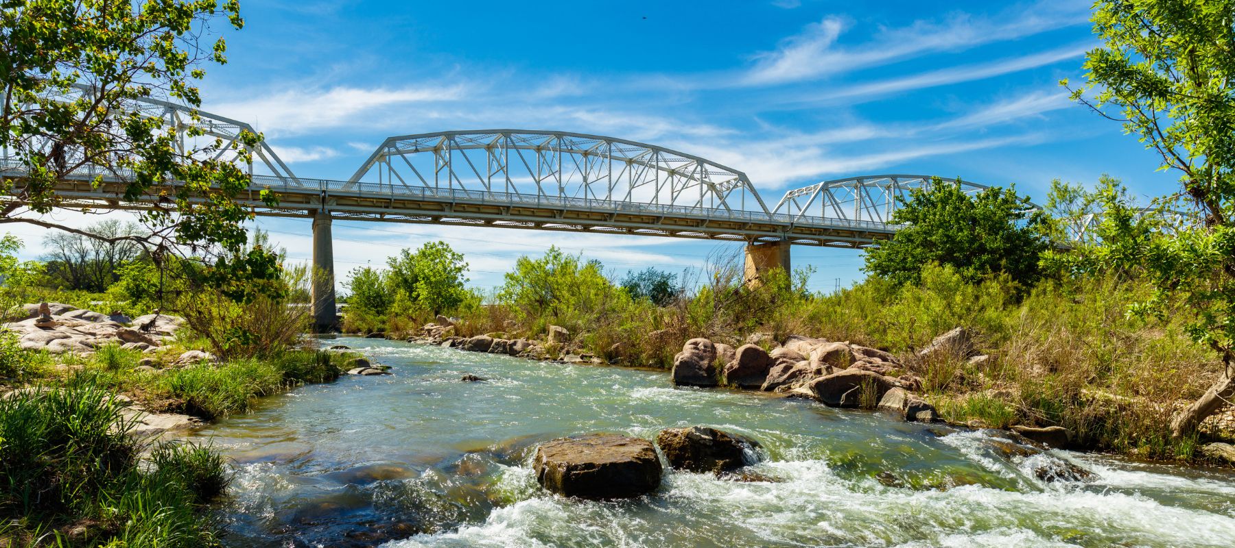 Steel truss bridge over a flowing river surrounded by greenery in Llano, Texas